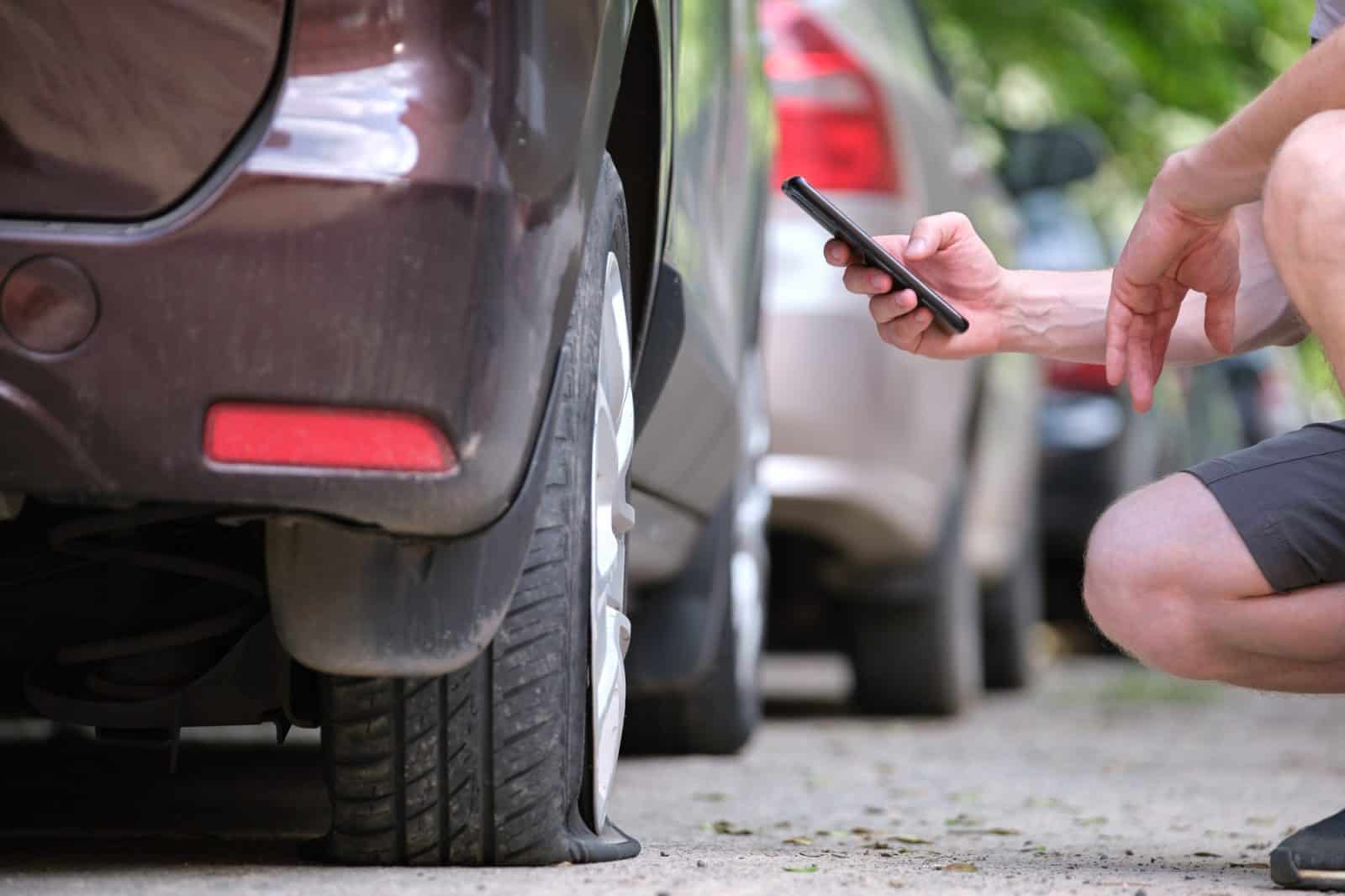 Driver calling road service for assistance having vehicle trouble with punctured flat tire